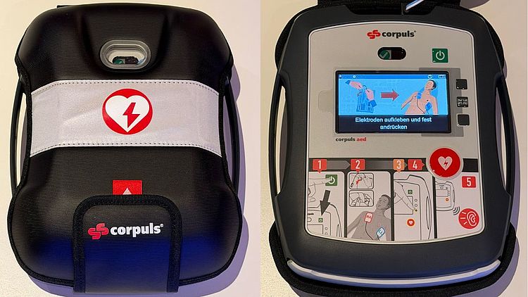 Das Bild zeigt zwei Ansichten eines automatisierten externen Defibrillators. Links ist eine geschlossene schwarze Tragetasche mit reflektierendem Streifen und einem Herzsymbol mit Blitz abgebildet. Auf der Tasche ist der Schriftzug „corpuls“ zu sehen. Rechts ist der Defibrillator aus der Tasche genommen dargestellt. Das Gerät hat ein rechteckiges Gehäuse mit Display, Bedientasten und Symbolen. Auf dem Bildschirm sind grafische Anweisungen zum Anbringen von Elektroden auf dem Oberkörper einer Person dargestellt. Unterhalb des Displays befinden sich nummerierte Bildsymbole, rechts eine große runde Taste mit Herzsymbol.